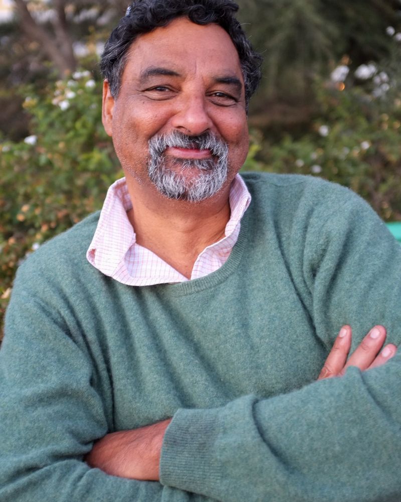 Paul Roy, smiling, sitting on a garden bench